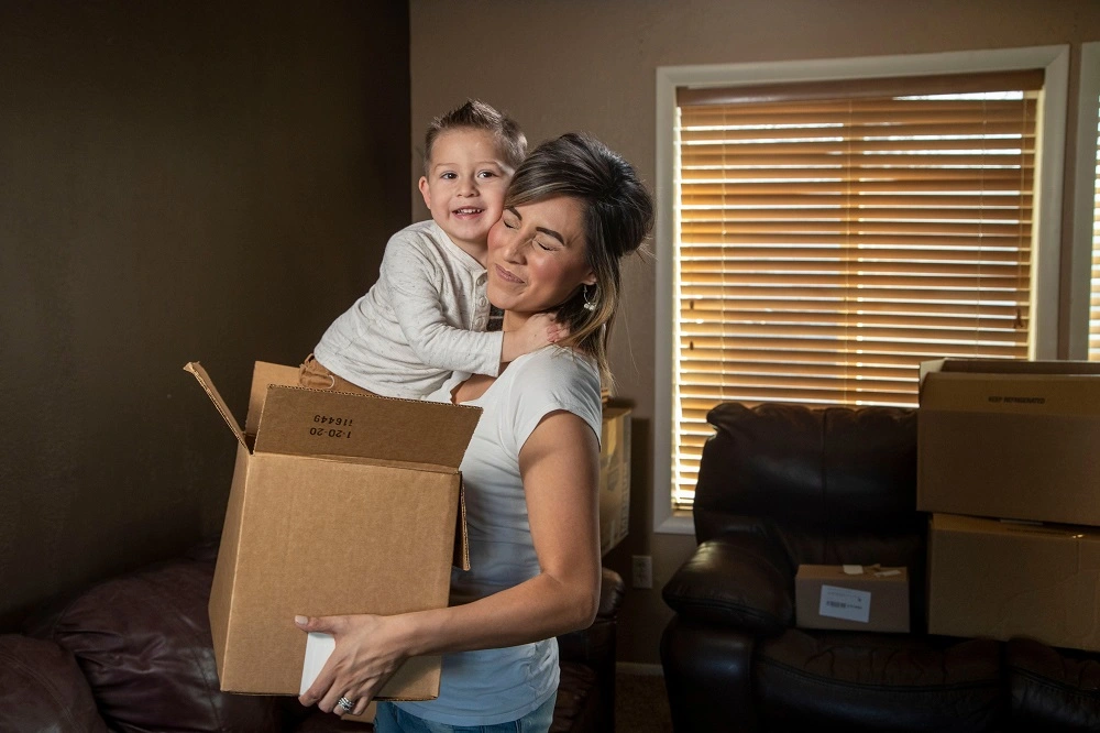 Mother carrying moving boxes with her son on her back