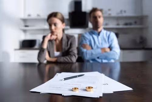 Couple sitting apart at a table with papers and wedding rings