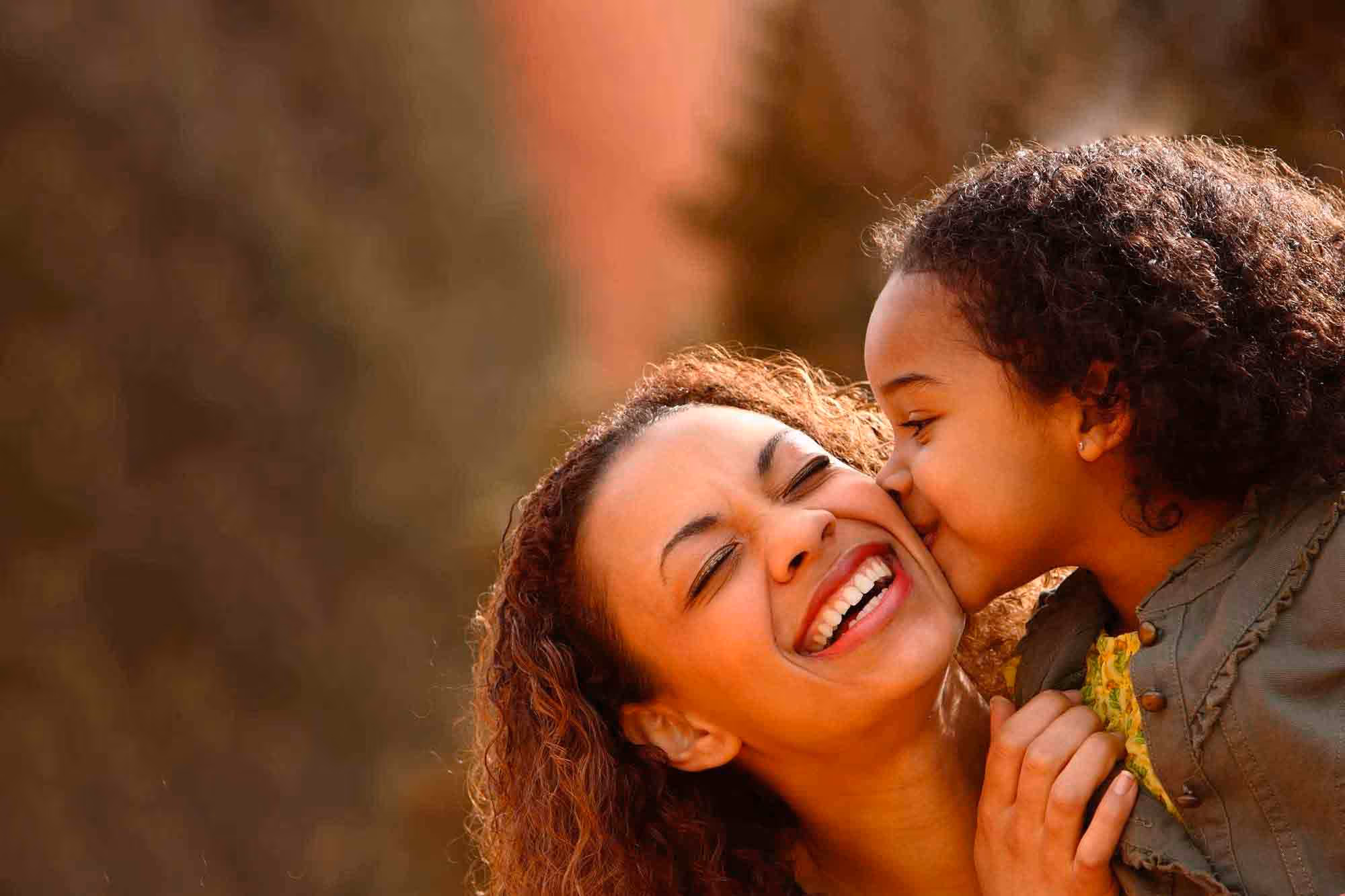Laughing mother kissed on the cheek by her young daughter