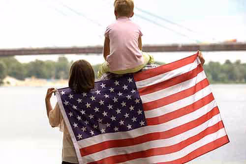 Two children holding an American flag by a river