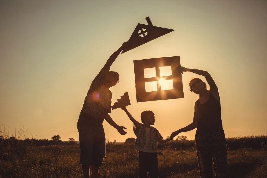 Family silhouette holding up a paper house at sunset